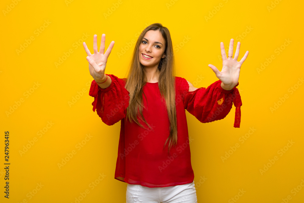 Young girl with red dress over yellow wall counting nine with fingers Young girl with red dress over yellow wall counting nine with fingers
