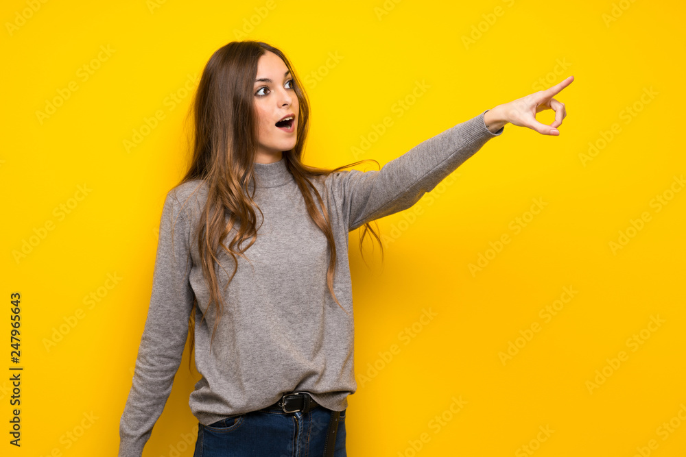 Young woman over yellow wall pointing away Young woman over yellow wall pointing away