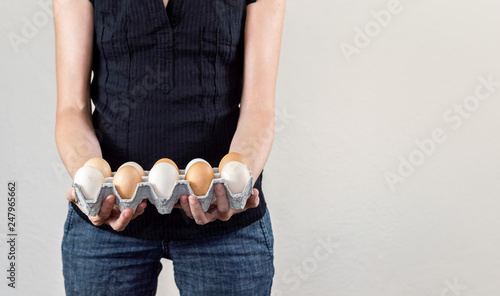 Caucasian woman with black shirt holding a cardboard egg box full of chicken eggs on a white background