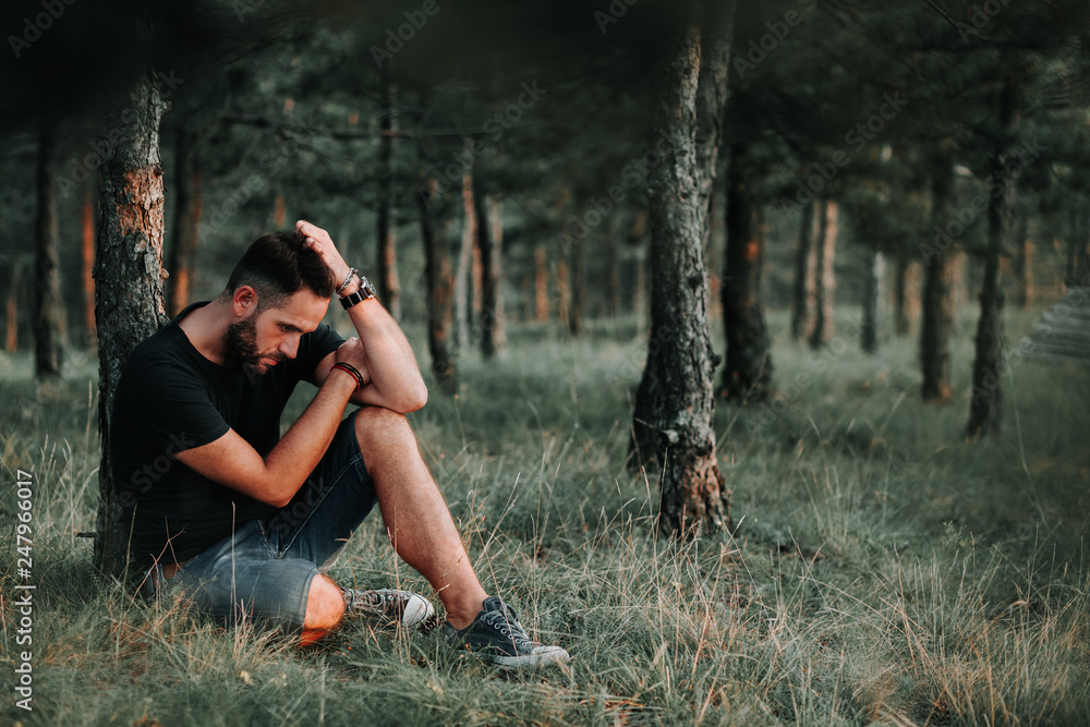 Young depressed man sitting alone in the forest