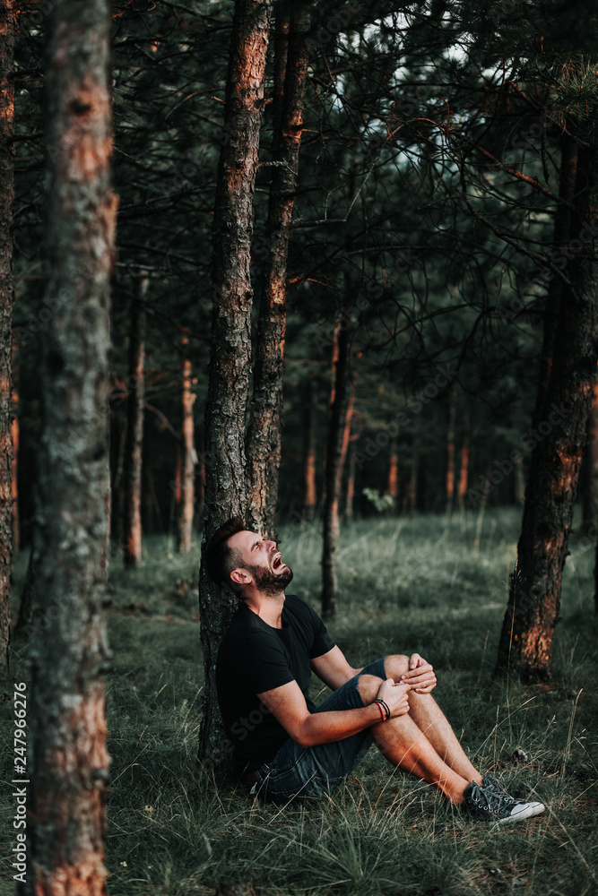 Young depressed man sitting alone in the forest Young depressed man sitting alone in the forest