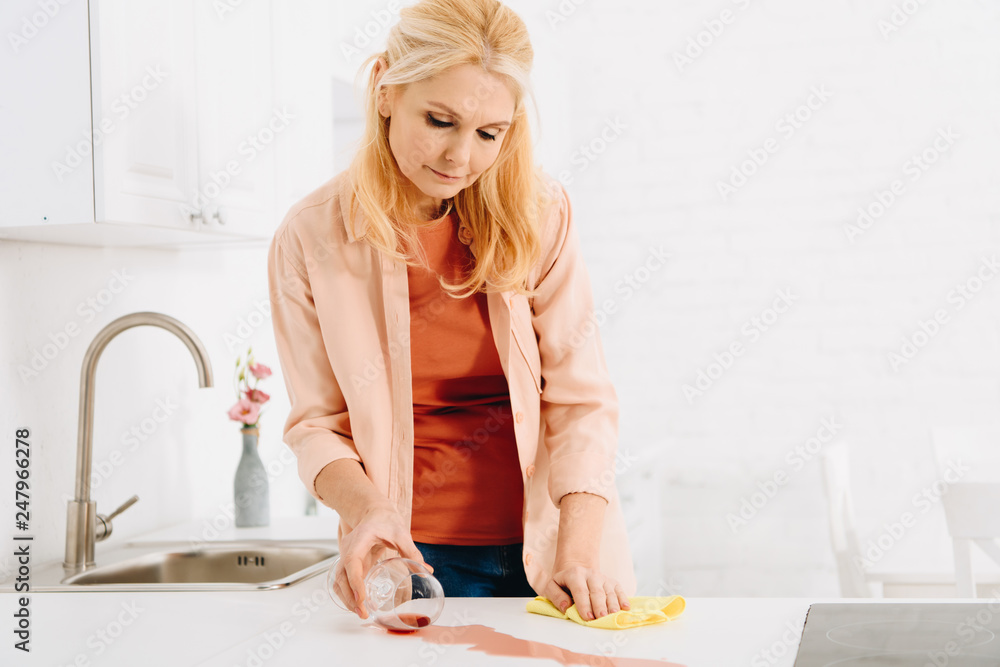 Attractive senior woman wiping wine spot with yellow rag Attractive senior woman wiping wine spot with yellow rag