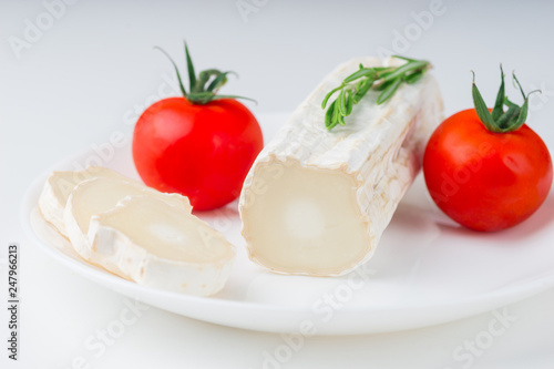 Tasty goat cheese with rosemary and tomato, on white table