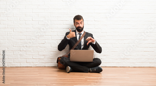 Businessman with his laptop sitting on the floor making good-bad sign. Undecided between yes or not