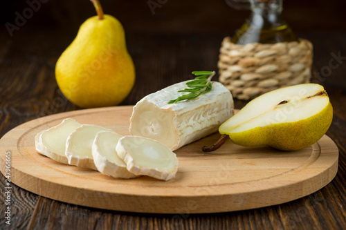 Sliced goats cheese rosemary and pear on wooden table.