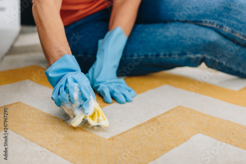 Cropped view of woman in blue rubber gloves cleaning carpet