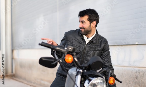 Young man on a motorbike pointing to the lateral © luismolinero