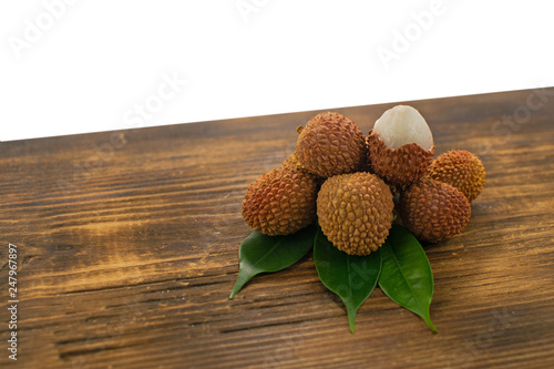 Fresh lychee and peeled showing the red skin and white flesh with green leaf on a wooden background. Lychi with leaves - tropical fruit. photo