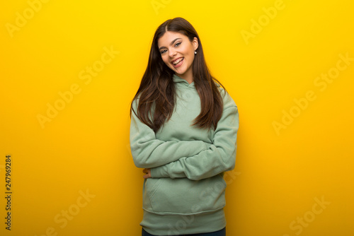 Teenager girl with green sweatshirt on yellow background keeping the arms crossed in frontal position © luismolinero