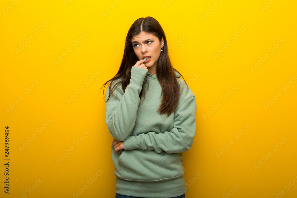 Teenager girl with green sweatshirt on yellow background having doubts while looking up Teenager girl with green sweatshirt on yellow background having doubts while looking up