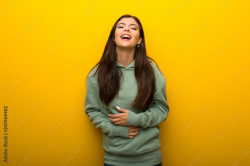 Teenager girl with green sweatshirt on yellow background smiling a lot while putting hands on chest Teenager girl with green sweatshirt on yellow background smiling a lot while putting hands on chest