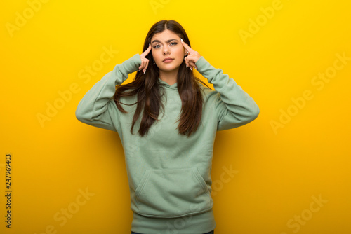 Teenager girl with green sweatshirt on yellow background having doubts and thinking © luismolinero