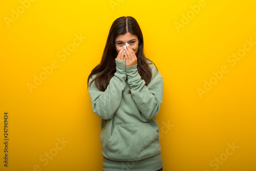 Teenager girl with green sweatshirt on yellow background smiling a lot while covering mouth © luismolinero