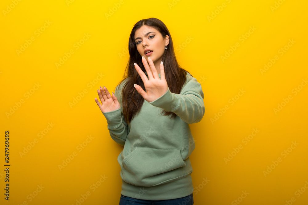 Teenager girl with green sweatshirt on yellow background is a little bit nervous and scared stretching hands to the front Teenager girl with green sweatshirt on yellow background is a little bit nervous and scared stretching hands to the front