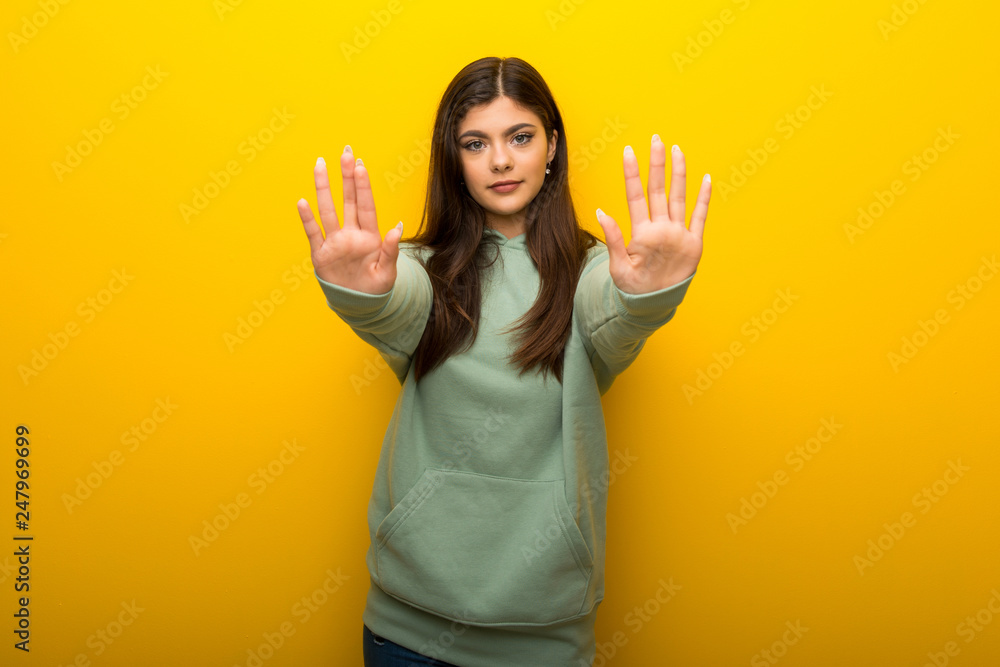 Teenager girl with green sweatshirt on yellow background making stop gesture for disappointed with an opinion Teenager girl with green sweatshirt on yellow background making stop gesture for disappointed with an opinion