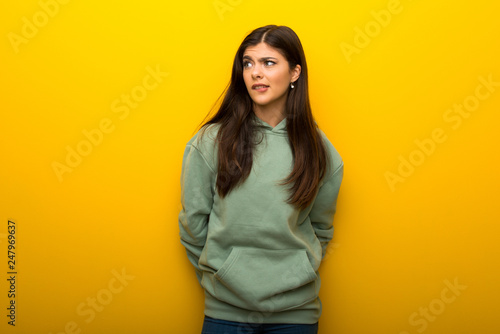 Teenager girl with green sweatshirt on yellow background is a little bit nervous and scared pressing the teeth © luismolinero