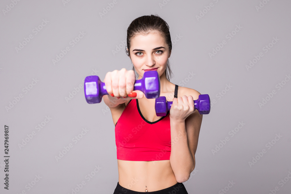 Young attractive happy woman in sport clothes with beautiful smile holding weight dumbbell doing fitness workout isolated on white background in healthy lifestyle concept Young attractive happy woman in sport clothes with beautiful smile holding weight dumbbell doing fitness workout isolated on white background in healthy lifestyle concept