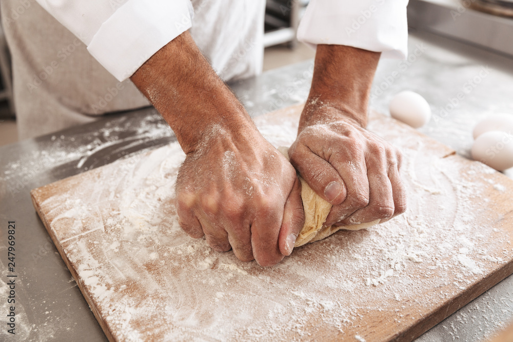 Closeup portrait of male hands making dough for loaf, on table at bakery or kitchen Closeup portrait of male hands making dough for loaf, on table at bakery or kitchen