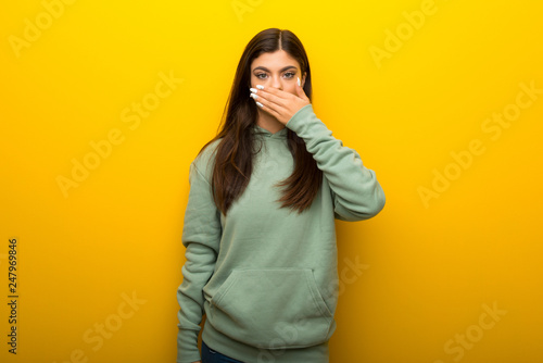 Teenager girl with green sweatshirt on yellow background covering mouth with hands for saying something inappropriate © luismolinero