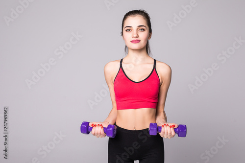 Young attractive happy woman in sport clothes with beautiful smile holding weight dumbbell doing fitness workout isolated on white background in healthy lifestyle concept © dianagrytsku