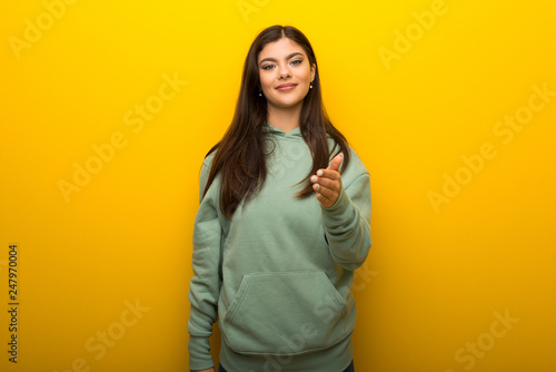 Teenager girl with green sweatshirt on yellow background shaking hands for closing a good deal