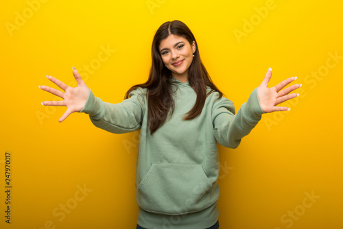 Teenager girl with green sweatshirt on yellow background presenting and inviting to come with hand © luismolinero
