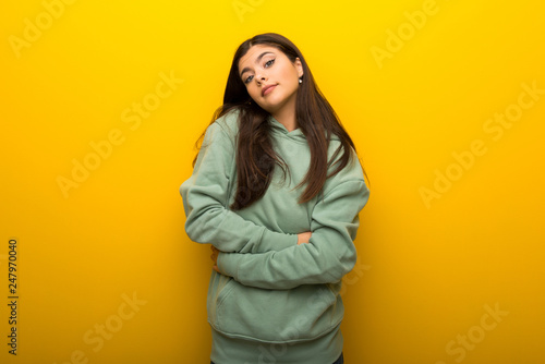 Teenager girl with green sweatshirt on yellow background making doubts gesture while lifting the shoulders © luismolinero