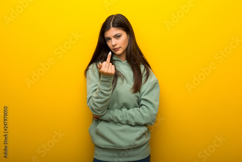 Teenager girl with green sweatshirt on yellow background making horn gesture © luismolinero
