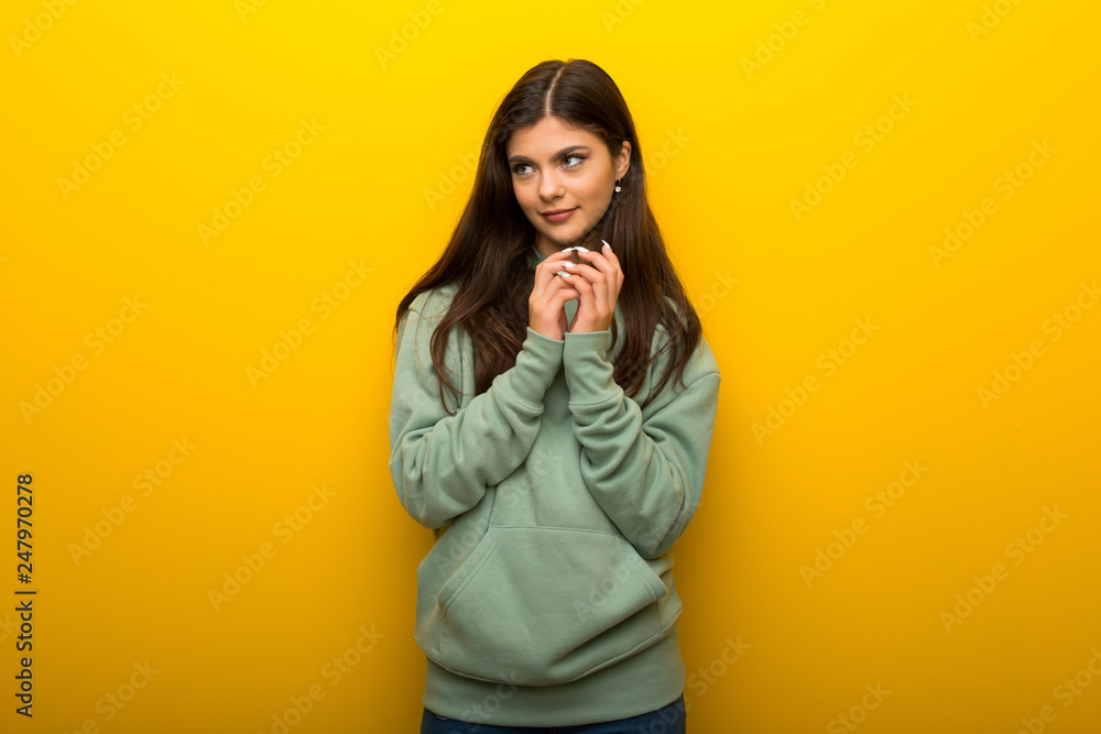 Teenager girl with green sweatshirt on yellow background scheming something Teenager girl with green sweatshirt on yellow background scheming something