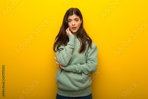 Teenager girl with green sweatshirt on yellow background surprised and shocked while looking right