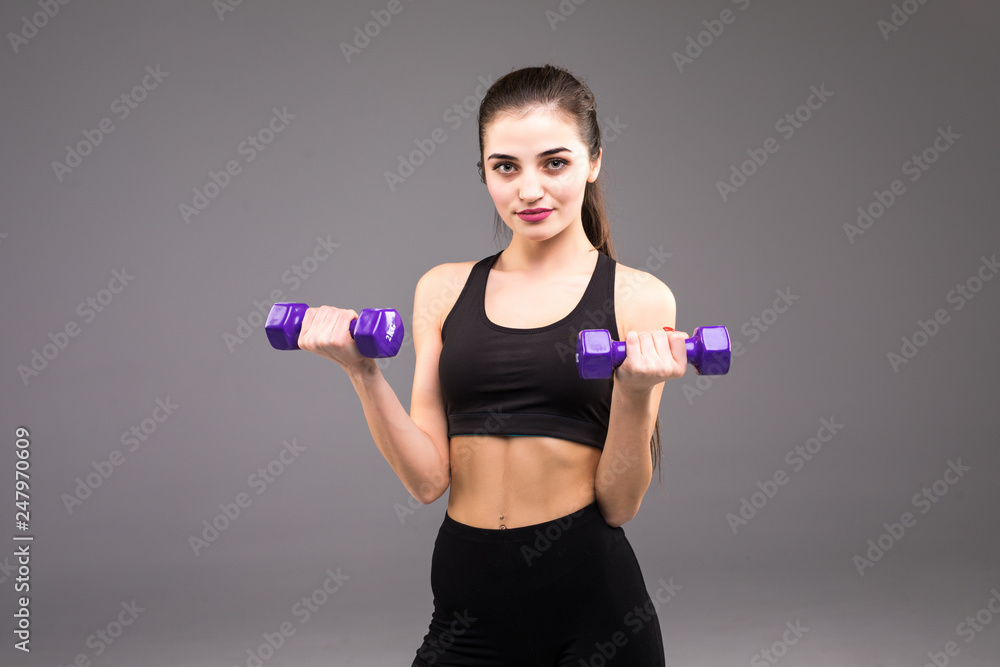 Young woman doing exercise with dumbbells. Portrait of sporty woman in training pumping up muscles hands on grey background. Strength and motivation Young woman doing exercise with dumbbells. Portrait of sporty woman in training pumping up muscles hands on grey background. Strength and motivation