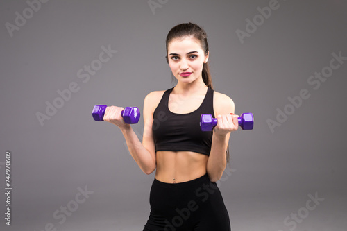 Young woman doing exercise with dumbbells. Portrait of sporty woman in training pumping up muscles hands on grey background. Strength and motivation