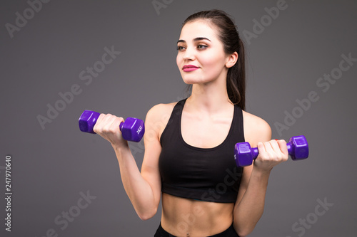 Portrait of cute concentrated woman practising and doing exercises with lifting small dumbbells up isolated over gray background