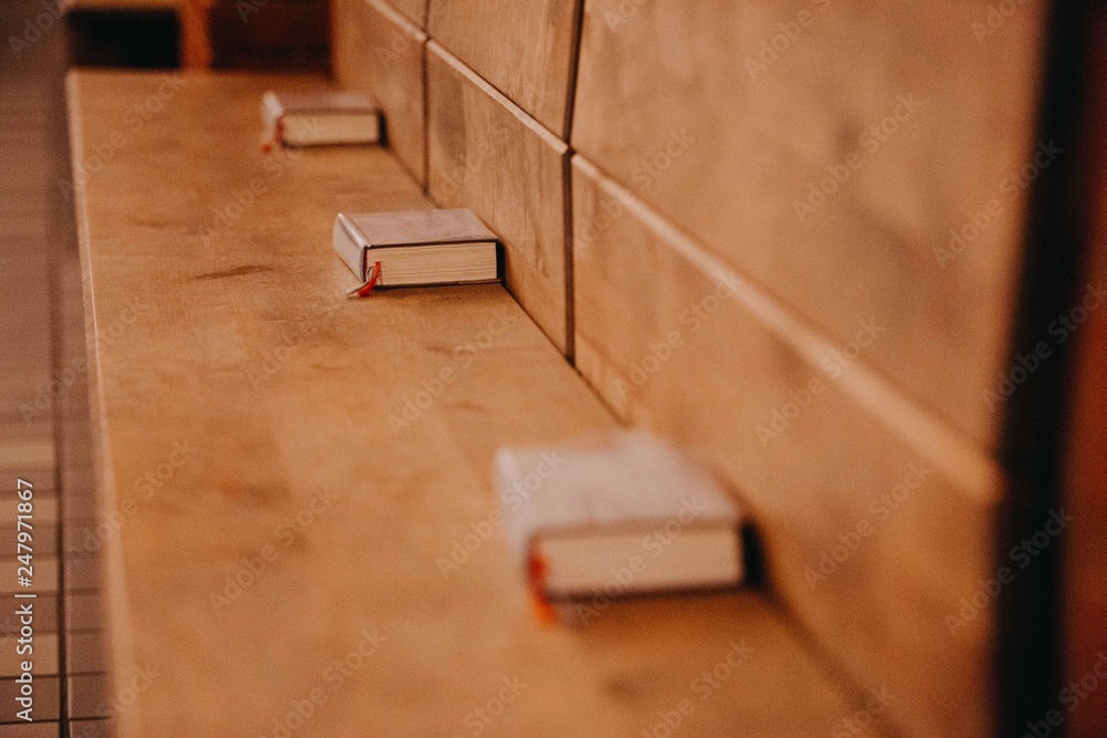 Bücher liegen geordnet auf einer Holzbank in einer Kirche oder Schule. 