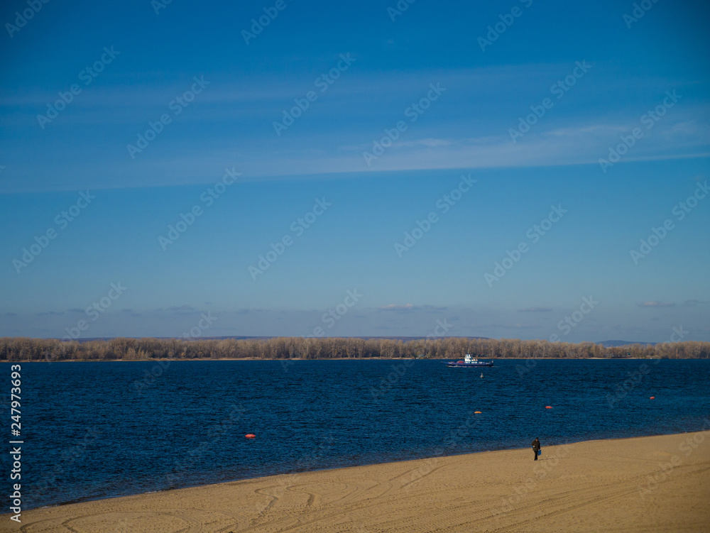 Beautiful solar autumn view of Volga River Embankment against the background of a blue palate with the lonely person on the beach.