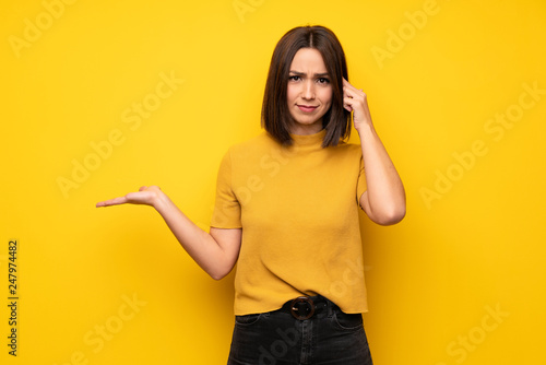 Young woman over yellow wall making the gesture of madness putting finger on the head