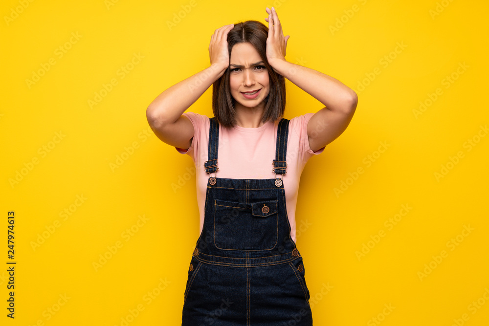 Young woman over yellow wall frustrated and takes hands on head Young woman over yellow wall frustrated and takes hands on head
