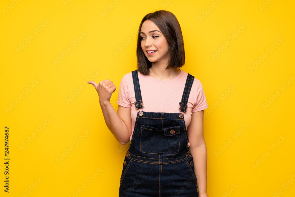 Young woman over yellow wall pointing to the side to present a product Young woman over yellow wall pointing to the side to present a product