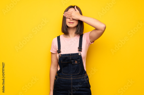 Young woman over yellow wall covering eyes by hands. Do not want to see something