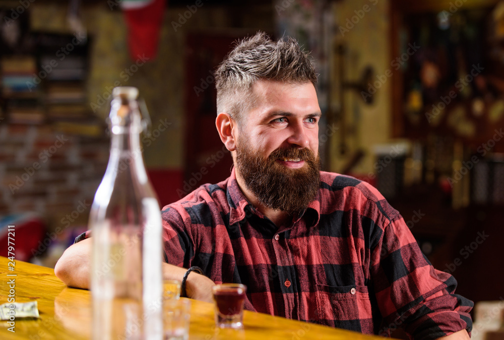 Friday evening. Hipster relaxing at bar. Bar relaxing place to have drink and relax. Man with beard spend leisure drinking strong alcohol. Drink for fun. Brutal hipster bearded man sit at bar counter