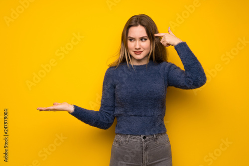 Teenager girl over yellow wall making the gesture of madness putting finger on the head