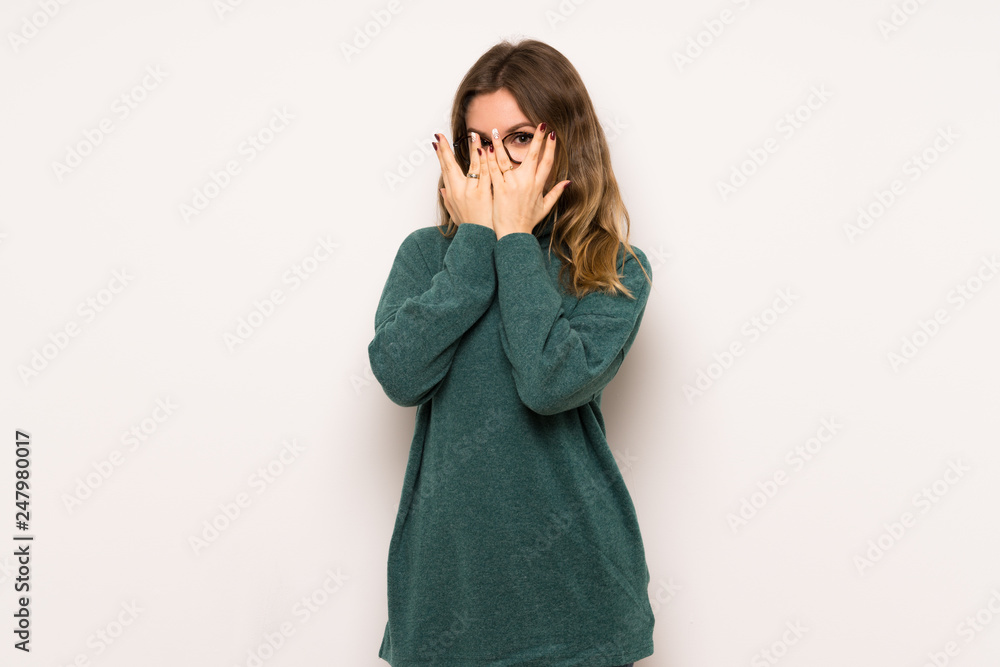Teenager girl over white wall covering eyes by hands and looking through the fingers Teenager girl over white wall covering eyes by hands and looking through the fingers