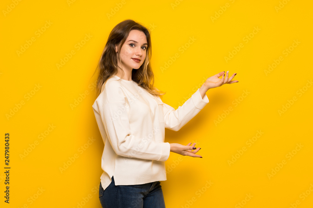 Teenager girl over yellow wall extending hands to the side for inviting to come Teenager girl over yellow wall extending hands to the side for inviting to come