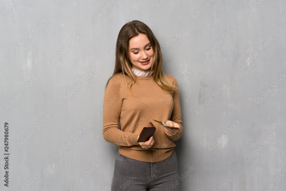 Teenager girl over textured wall holding a wallet Teenager girl over textured wall holding a wallet