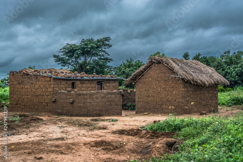 View of traditional village, house thatched on roof and terracotta walls, dramatic cloudy sky as background