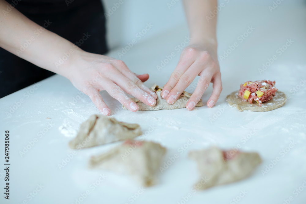 The girl carefully and gently sculpts meat pies. hands closeup on the table with flour
