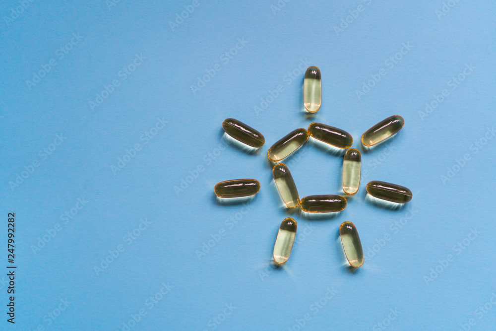 Close up capsules of fish fat oil in the sun shape, omega 3, vitamin e on the blue background. Healthy food diet. Nutritional supplement Close up capsules of fish fat oil in the sun shape, omega 3, vitamin e on the blue background. Healthy food diet. Nutritional supplement
