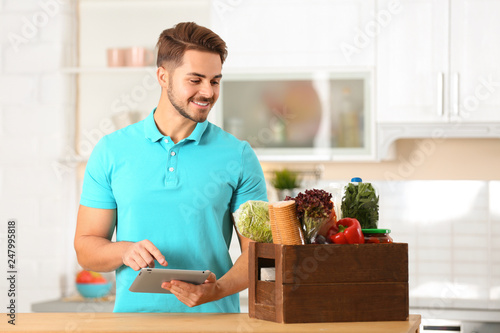 Young man with tablet PC and products in kitchen. Food delivery service