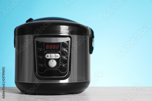 Modern electric multi cooker on table against color background. Space for text