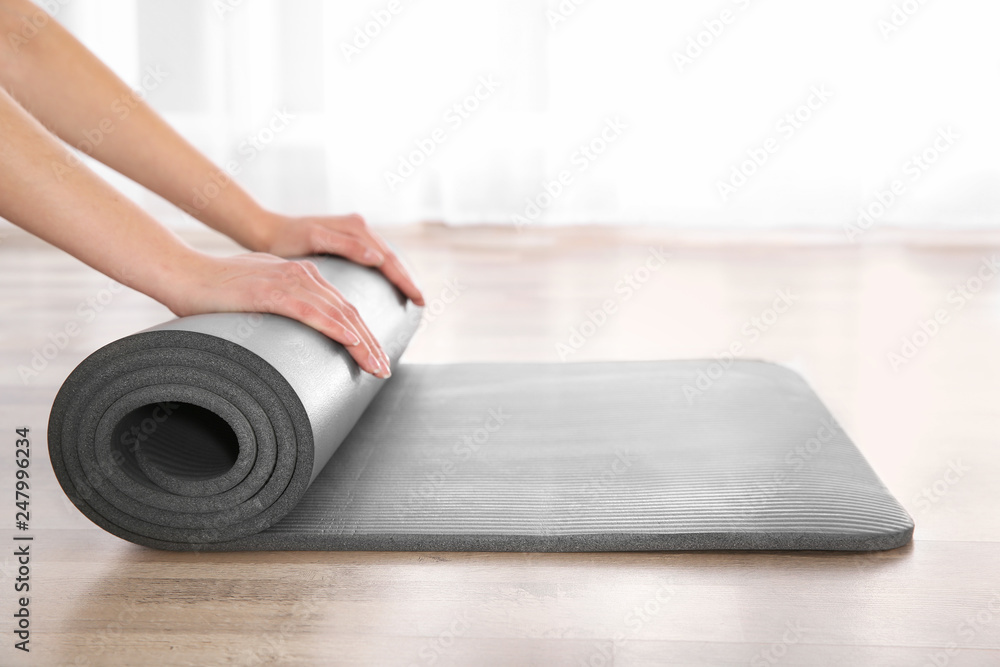 Fototapeta premium Woman rolling yoga mat on floor indoors, closeup